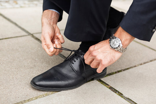 Businessman tying his shoe on pavement, close-up