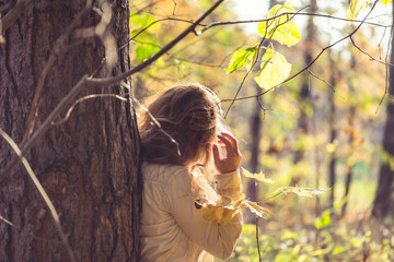 Female in headphones standing near big maple tree in park and listen sounds or music in the autumn forest. Concept. Indian summer season