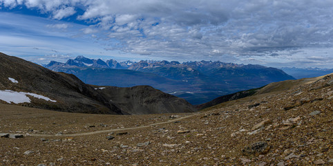 Hiking trail through a panoramic Rocky Mountain landscape with a white clouds, mountains and hills.