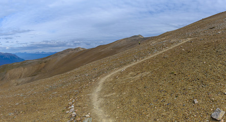 Hiking trail through a panoramic Rocky Mountain landscape with a white clouds, mountains and hills.