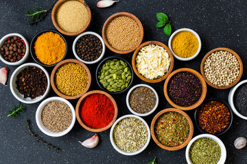 Variety of colorful spices, herbs, and seeds on black stone background
