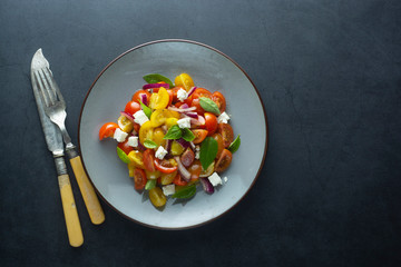 Colorful cherry tomatoes and basil salad in a plate, dark background. Healthy, summer food.