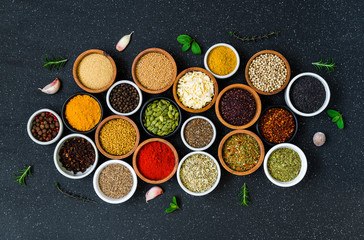Variety of colorful spices, herbs, and seeds on black stone background
