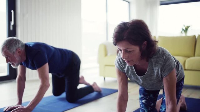 A senior couple indoors at home, doing exercise indoors. Slow motion.