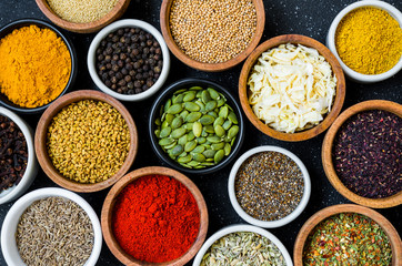 Variety of colorful spices, herbs, and seeds on black stone background