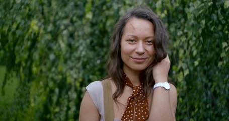 lady with white wristwatch smiles against green tree