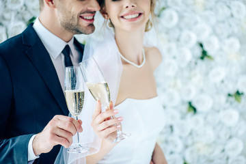 cropped view of bride and bridegroom clinking with champagne glasses