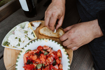 The man has an Italian style snack salad with mozzarella tomatoes and ciabatta bread outside on a wooden bench