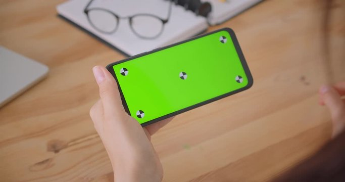 Closeup back view portrait of young female doctors hand playing advt on phone with green chroma key screen indoors in office