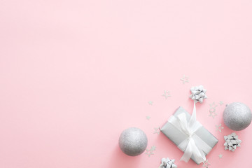 Christmas decorations, stylish silver gift boxes, baubles, confetti on pastel pink background. Minimal flat lay style composition, top view, copy space. Christmas fashion glamour concept