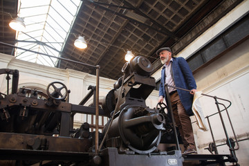 Fototapeta na wymiar Worker standing on top platform of an old vintage press for newspaper printing