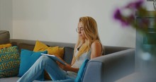High quality 4k 12bit footage of Beautiful girl using Tablet PC sitting on couch at home. Woman surfing web, social networks, looking something in online shop. Cinematic look