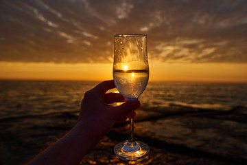 morning energy. hand holding glass of white wine and with sea and beautiful sunrise at background, close-up. Holiday, day off morning relaxed mood concept