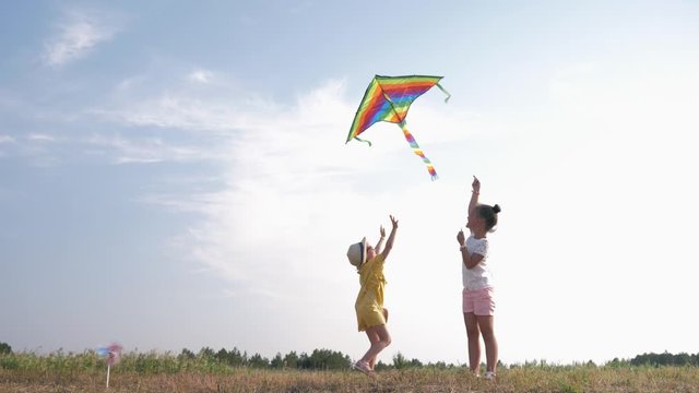 little happy girlfriends play with a kite, beautiful girls actively spend time outdoors playing with an air toy in a forest glade during a country vacation, children relationship