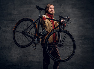 Modern bearded hipster in red sweater is holding his bike while posing for photographer.