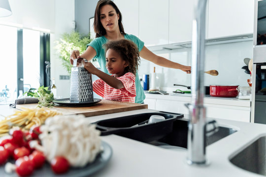 Mother and daughter cooking in kitchen together grating cheese