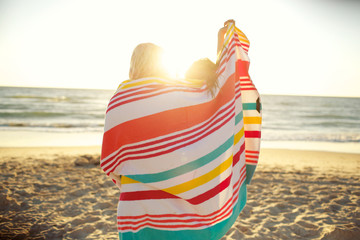 Two girls standing on beach sharing beach towel