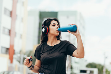 Beautiful young woman using headphone listening to music and drinking water outdoors