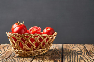 Full wicker basket of tomatoes lies on old rustic wooden table. Space for text