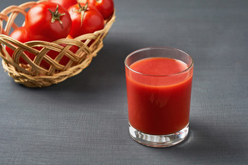 Full glass of fresh juice and wiker wooden basket full of ripe tomatoes  lies on dark concrete