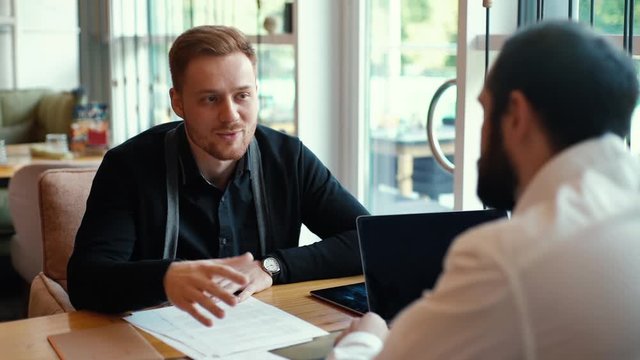 Candidate for job presents himself to potential employer in relaxed cafe environment. HR manager having job interview listening with young man in cafe. Subordinate reports to his boss in slow motion