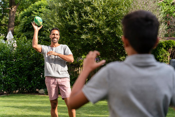 Father and son playing with American football in garden