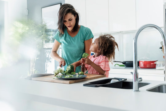 Mother and daughter cooking in kitchen together cutting broccoli