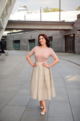 Beautiful middle-eged smiling woman model with dark hair wearing light clothes,posing on the street in summer day 