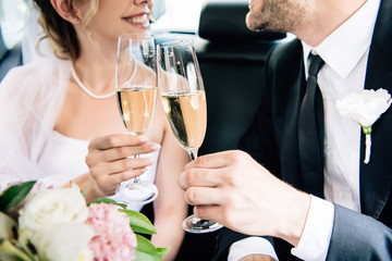cropped view of bride and bridegroom clinking with champagne glasses