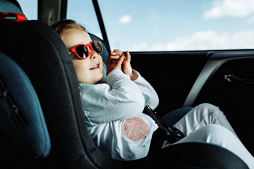 little cute girl in cap sitting in the car in child safety seat - 287827980