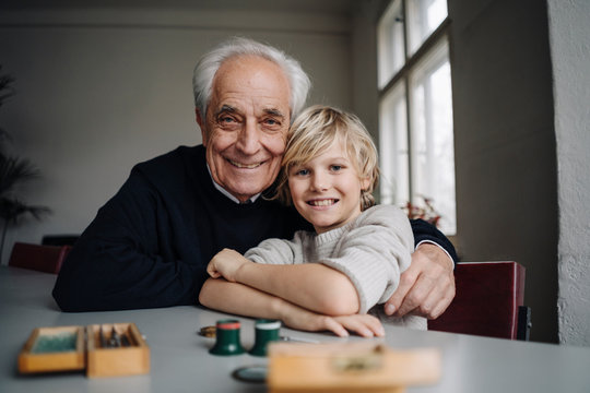 Portrait of happy watchmaker and his grandson sitting at table