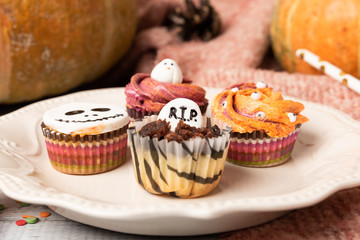 Festive Halloween cupcakes decorated colored decorations witch hat, orange cream, the face of a ghost. Wooden background with pumpkin and copy space, selective focus.