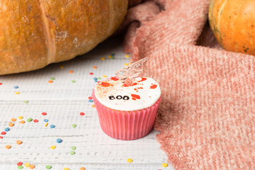 Festive Halloween cupcakes decorated colored decorations witch boo text on hatchet. Wooden background with pumpkin and copy space, selective focus.
