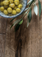 Pitted olives in a bowl with leaves on wood background with copy