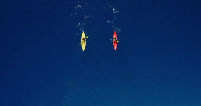 Aerial view of two kayakers paddling together in pristine dark blue ocean water on a sunny day, young adventurous couple kayaking together