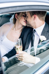 attractive bride and handsome bridegroom kissing and holding champagne glass