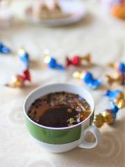Cup of black flower tea on the table with candies in wrappers, close up, selective focus