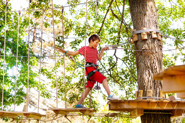 Boy walk on suspended rope bridge between trees