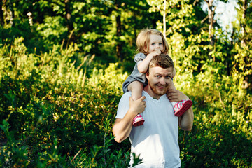 Obraz premium Dad carries his daughter on his shoulders across the field at sunset.