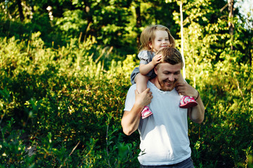 Fototapeta premium Dad carries his daughter on his shoulders across the field at sunset.