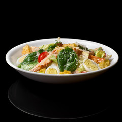 Tasty appetizing fresh salad Caesar with chicken, tomatoes, the eggand cheese parmesan in bowl on black background. View from above.