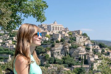Cheerful young blond woman at Gordes old hilltop town surrounded by mountains, Provence, France