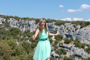 Blond emotional female traveler at Canyon Gorges de la Nesque, gray cliffs with green forest in summer sunny day