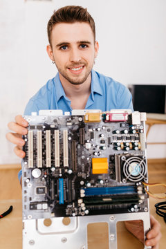 Portrait of smiling technician holding the mainboard of a computer