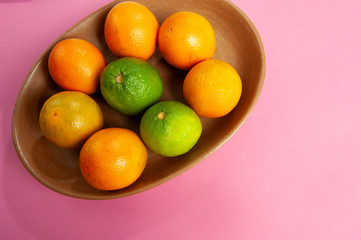 Clay bowl, rustic, handcrafted, with orange, lemon fruit. Cassis color background. From above. Text space.