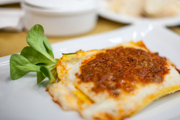 Lasagna served on a white plate with salad. Italian food.
