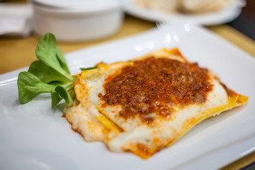 Lasagna served on a white plate with salad. Italian food.
