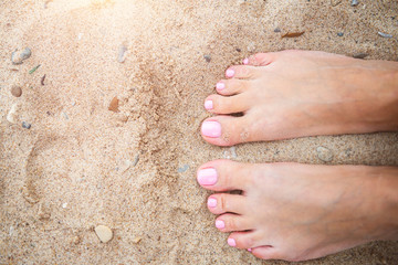Young lady is showing her light pink pedicure nails on sandy beach backgroung