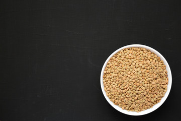 Organic green lentils in a white bowl on a black background, overhead view. Flat lay, top view, from above. Copy space.