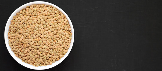 Organic green lentils in a white bowl on a black background, view from above. Flat lay, top view, overhead. Copy space.